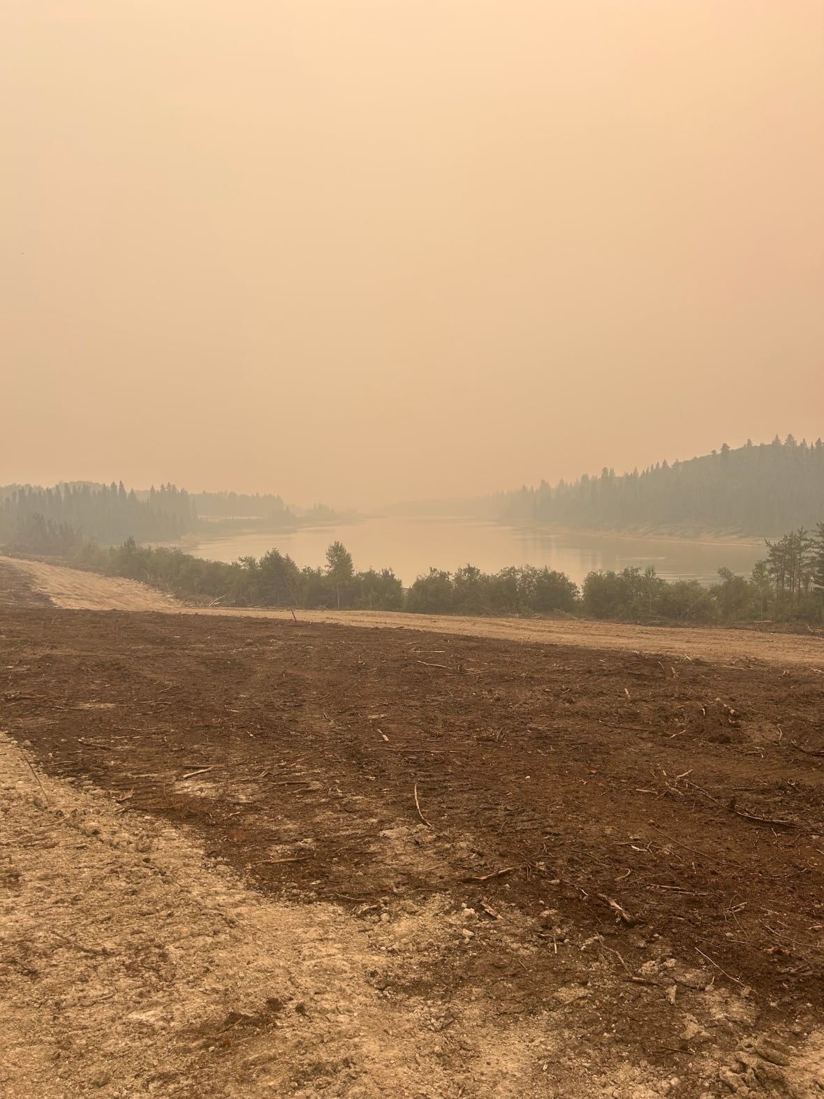 Brown hazy sky along a dirt trail next to a body of water.