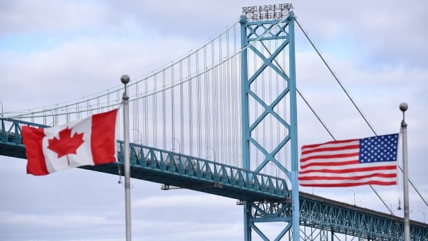 Canadian and American flags fly alongside a suspension bridge.