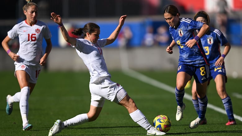 A female soccer player stretches out her right leg to kick the ball in front of an opponent.