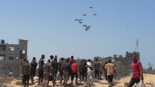 Several men watch as aid packages fall from the sky by parachute