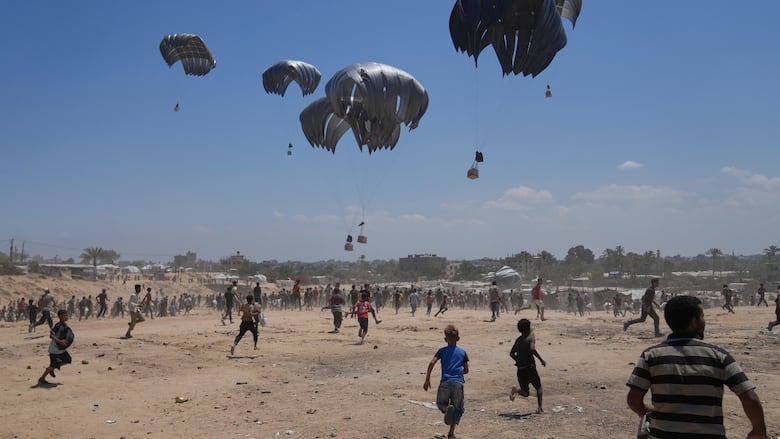 People rush to collect aid dropped in by parachute.
