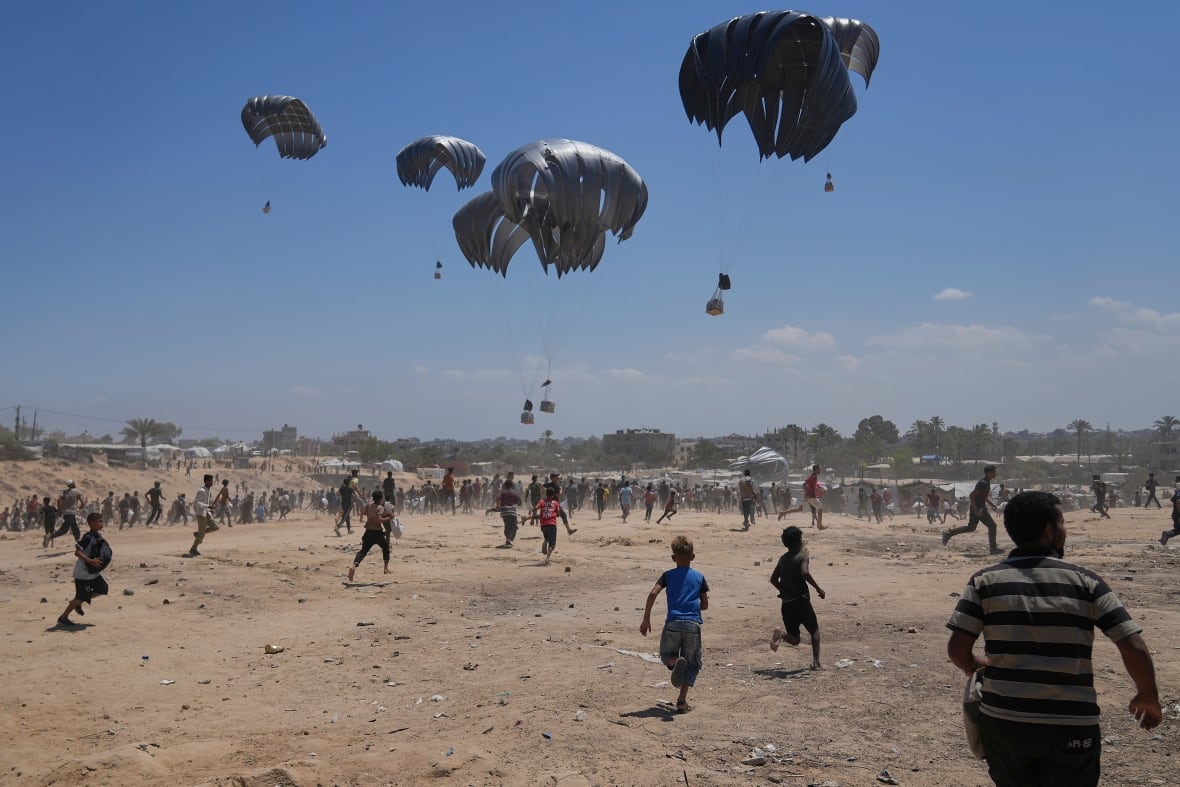 People rush to collect aid dropped in by parachute.