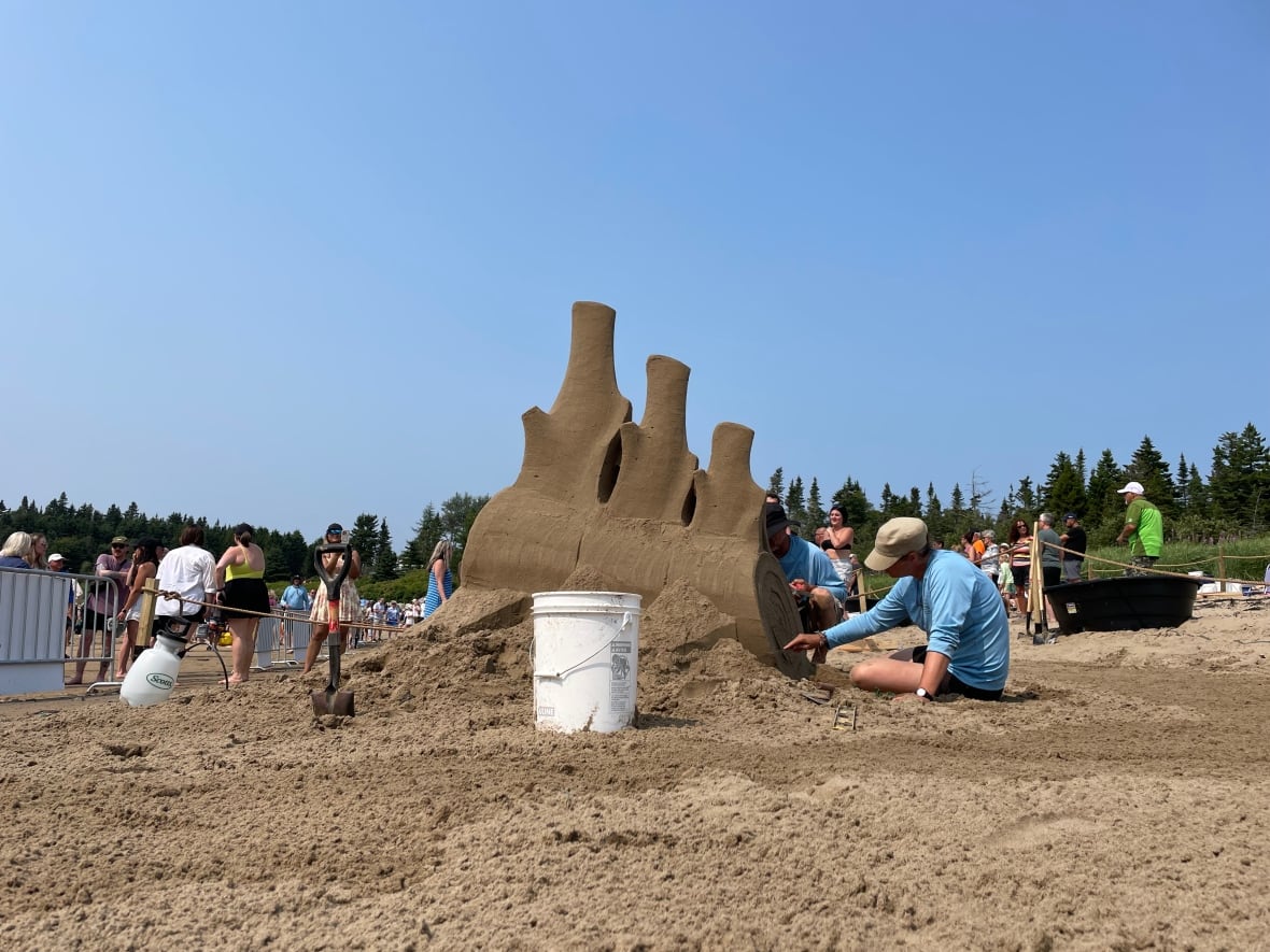 A man working on a sand sculpture of whale vertebrae on a beach.