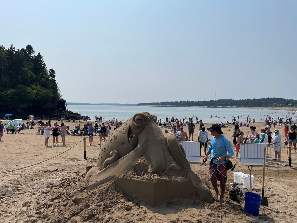 A sand sculpture of an octopus on a crowded beach with the ocean in the background.