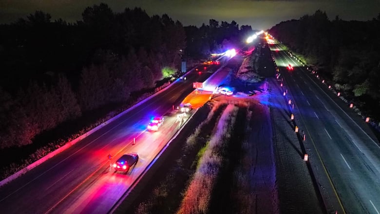 The photo shows a nighttime aerial view of a serious crash scene on Highway 1 in Langley, B.C. Several police vehicles with flashing lights are parked across the westbound lanes.