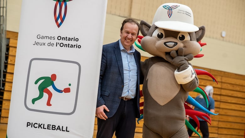 A man stands next to a chipmunk mascot in a gymnasium.
