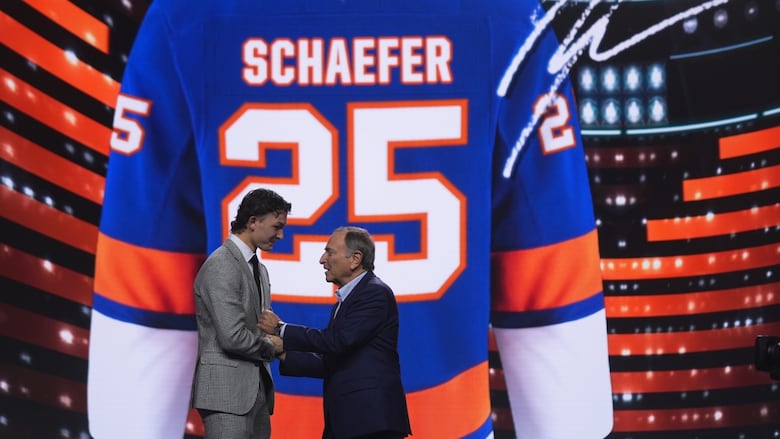 Two males shake hands on a stage with a hockey jersey projected in the background.