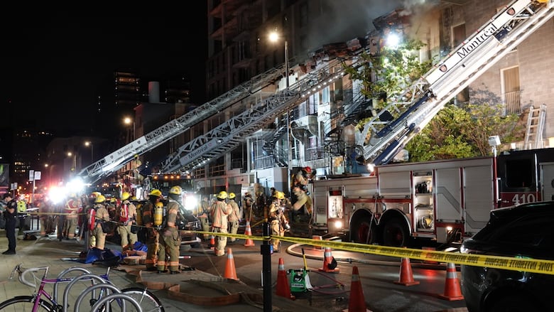 Several firefighters and ladder trucks are seen as smoke emanates from a three-storey building.