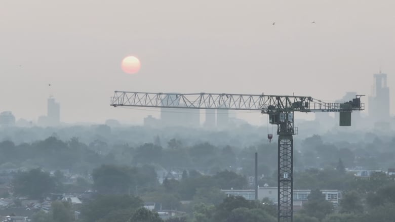 A construction crane is seen with the background of a hazy sky and a bright red sun