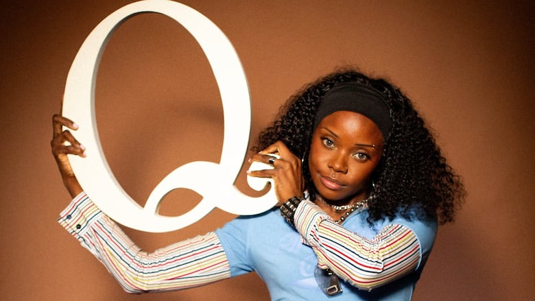 Headshot of BAMBII posing with a large letter Q cut-out.