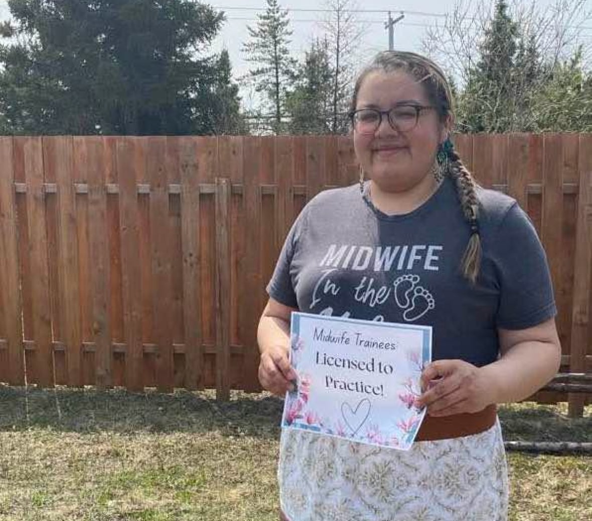 A Cree woman wearing a shirt that says 'midwife' while holding a document. 