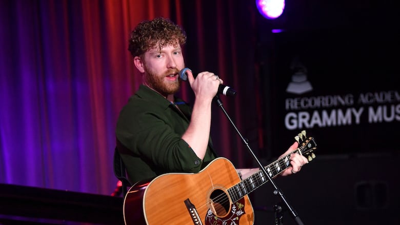 A man with red hair plays the guitar while wearing a dark shirt.