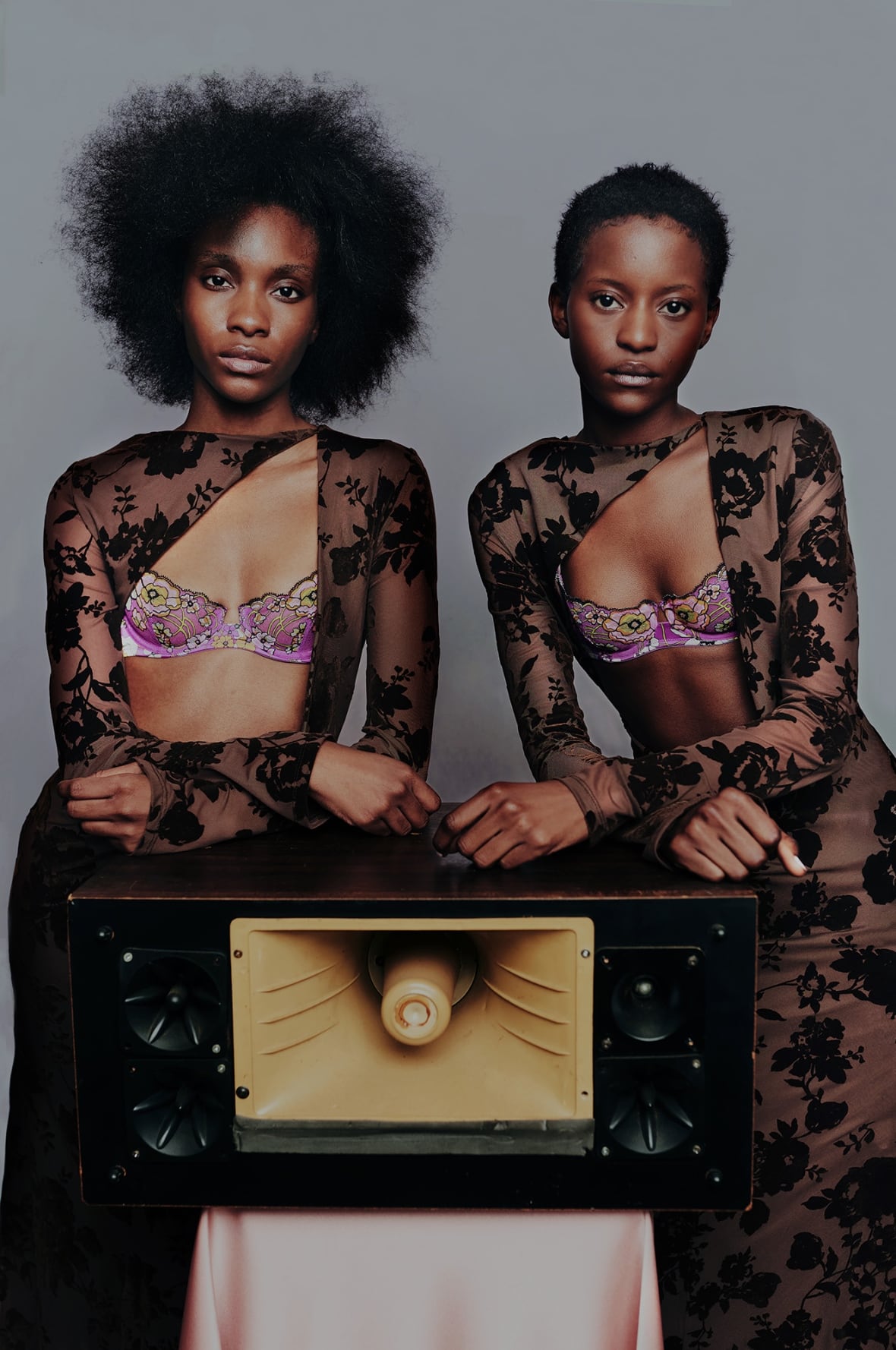 Two women wearing printed dresses stand over a loudspeaker.