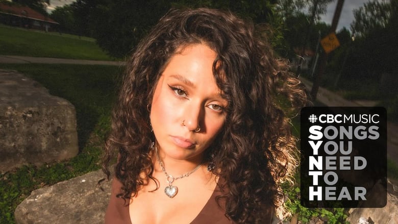 A photo of Ruby Waters wearing a brown v-neck shirt and a heart pendant. The CBC Music logo and text reading Songs You Need to Hear appear in the lower right corner. 