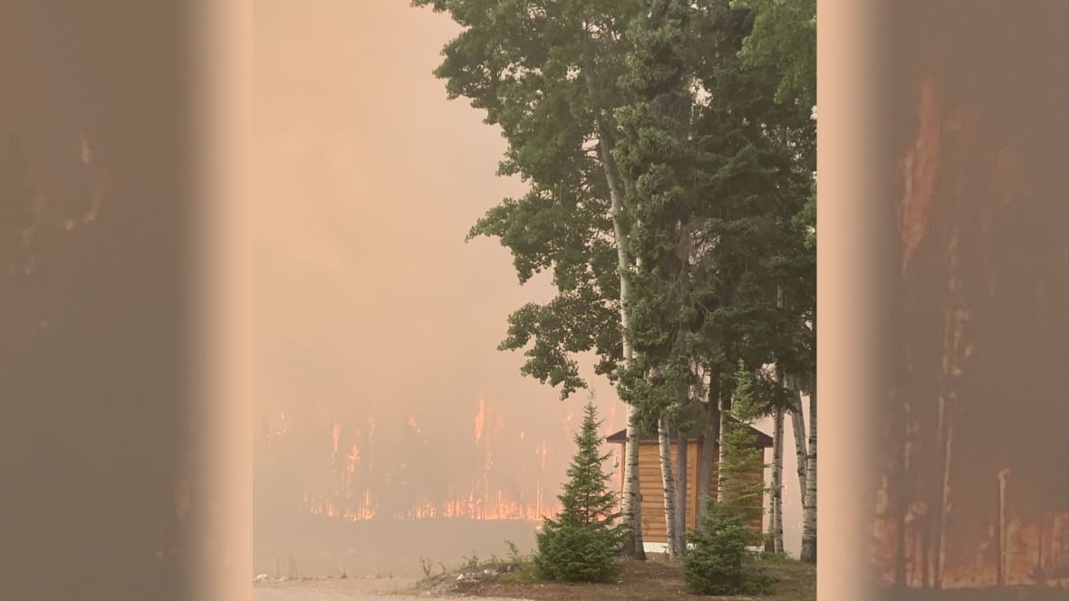 Flames can be seen burning a forest near a cabin structure.