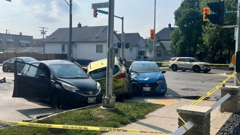 Three vehicles are seen damaged in a crash, with police tape and vehicles nearby.