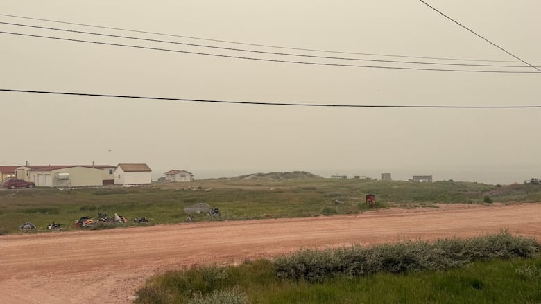 A hazy sky over a small community with a dirt road and a few houses.