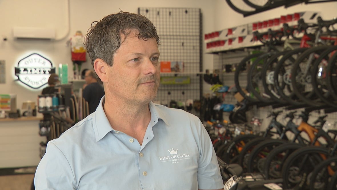 A white man with brown hair in a bike store. He's wearing a sky blue polo.