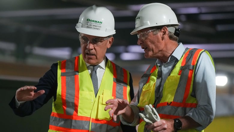 two men in high-vis vests and hard hats speak together.