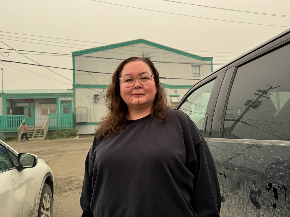 A women standing next to a car, with a building and a hazy sky in the background.