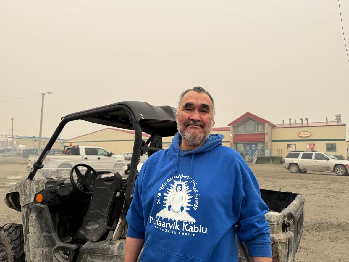 A man standing in front of an ATV with a building and a hazy sky in the background.