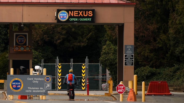 A bicyclist in a blue shirt with a red backpack approaches the Nexus lane at a border crossing checkpoint.