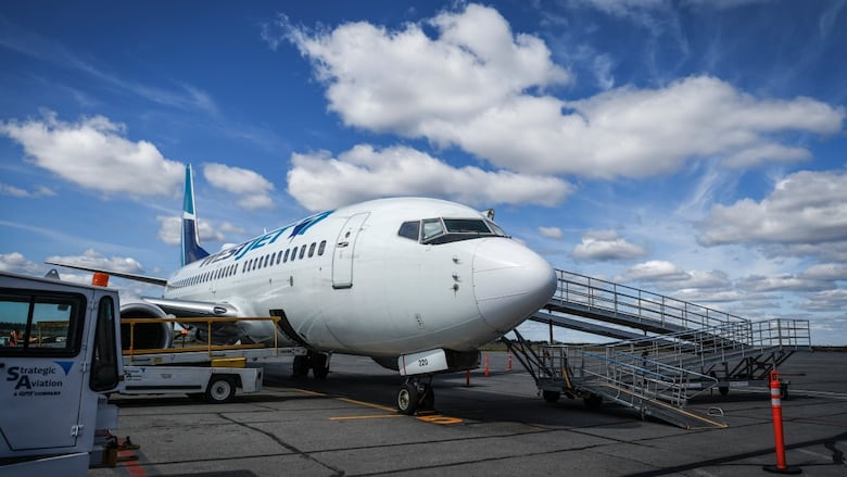 A plane is seen sitting on the tarmac under a blue sky with clouds. 