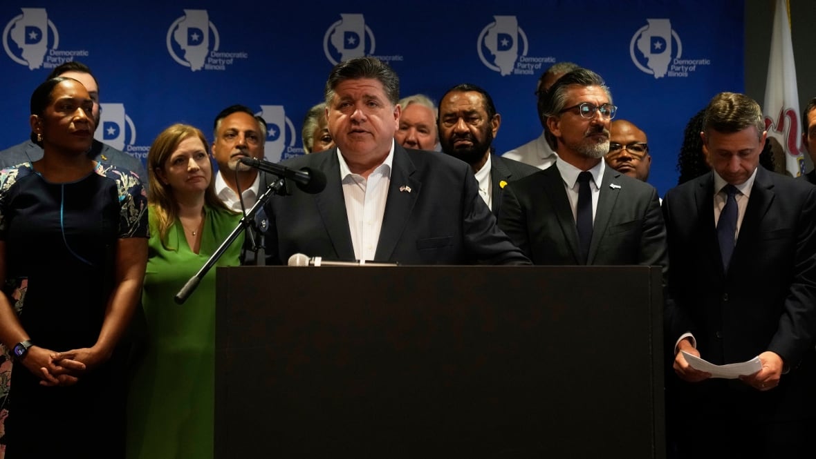 Illinois Gov. JB Pritzker represents a podium, with several Democtat State legislature in Texas behind him. 