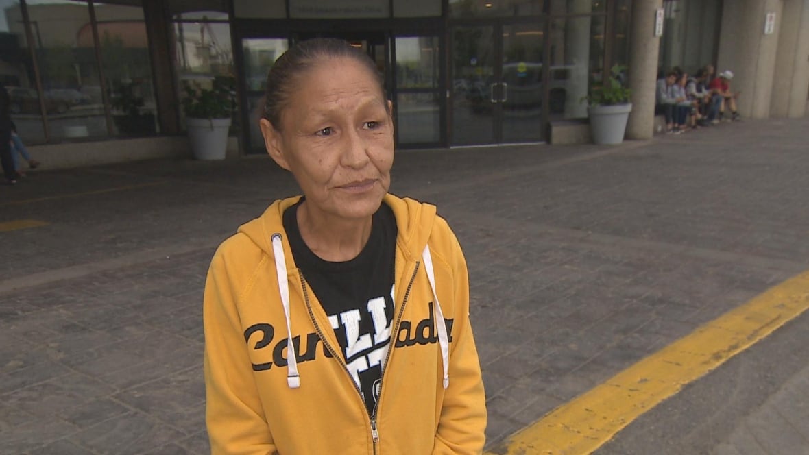 Bonnie Janvier stands in a yellow hoodie that says Canada  over a black t-shirt with white lettering.  