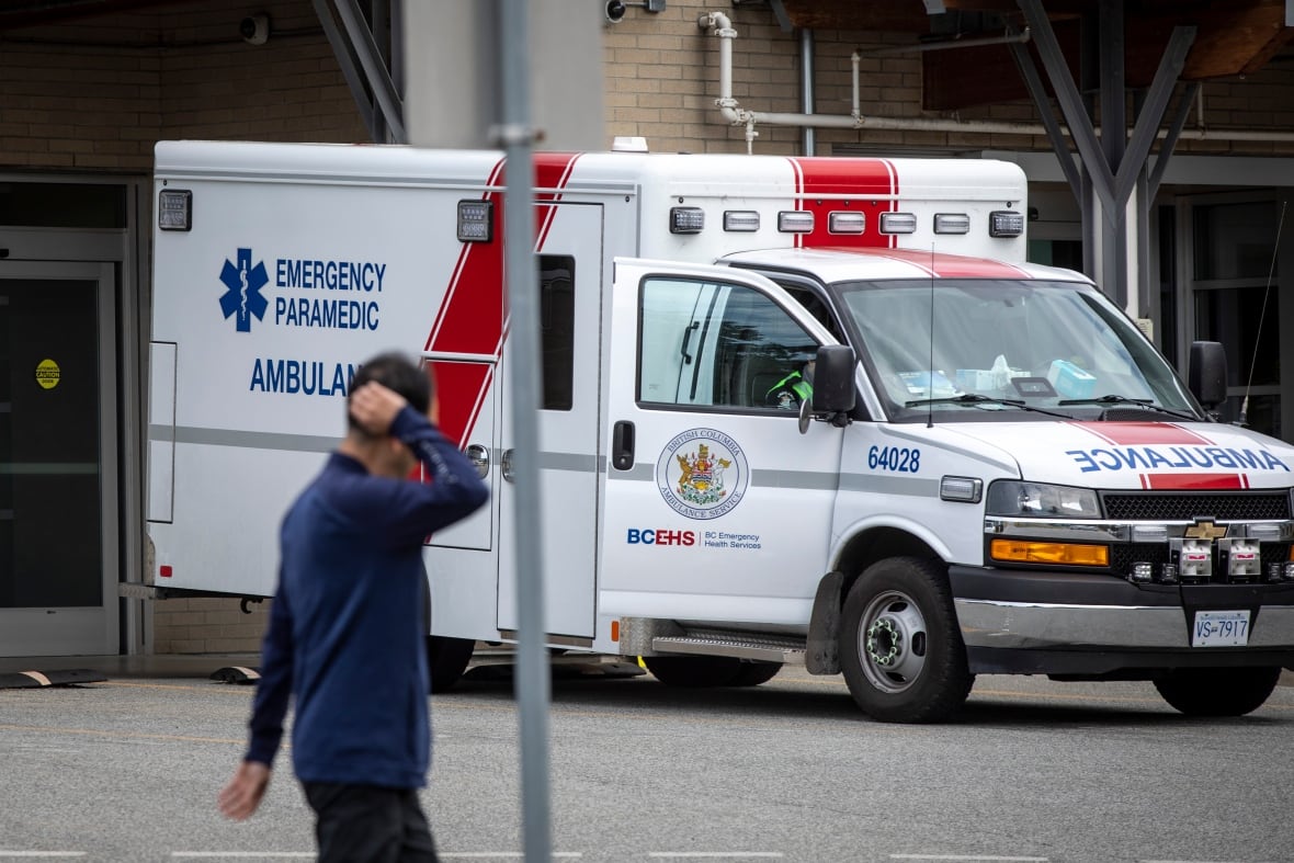 A man scratches his head as he walks by an ambulance.