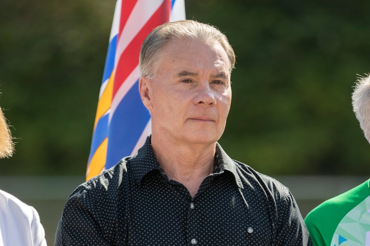 A man wearing a black dotted shirt looks on during a sunny day.