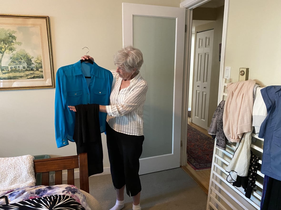 A woman holds a dress in a bedroom.