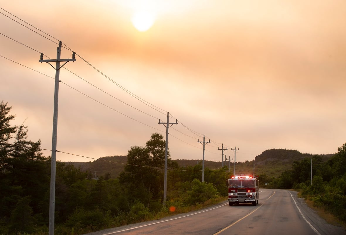 El solitario camión de bomberos camina por la carretera del bosque contra el cielo rojo ahumado.