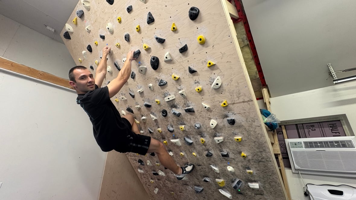 A rock climber is seen posing on his garage rock climbing wall.