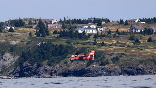 An orange plane flying over a body of water.