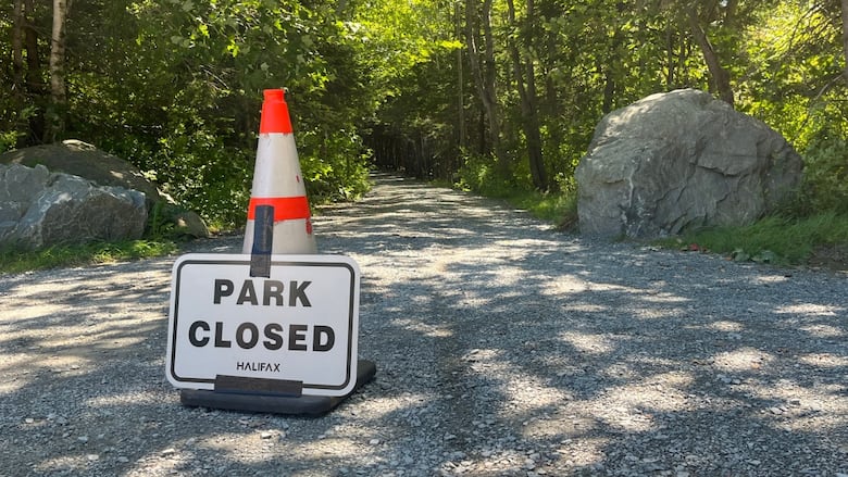 A pylon sits on a gravel trail with a sign attached that says Park Closed.