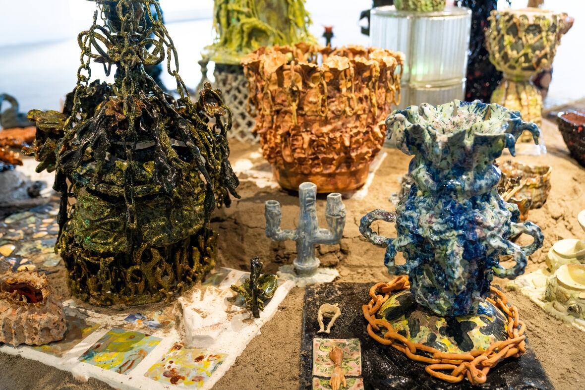 The closeup photograph shows an assortment of ceramic vases that look like plant life sitting on a mound of sand.