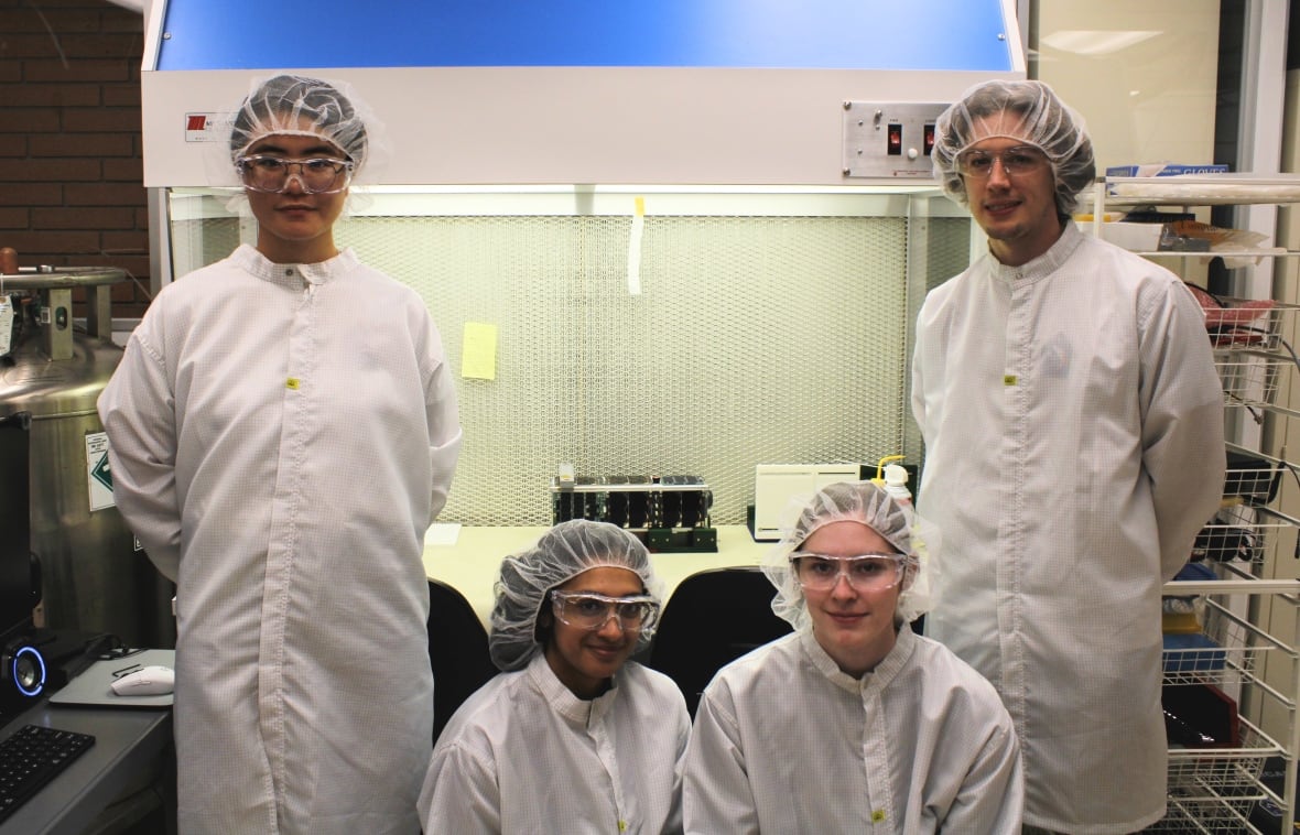 CalgaryToSpace 团队的四名成员在 CubeSat 卫星前合影。