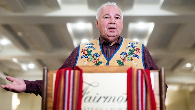 A man stands at a podium which is draped with a Métis sash.