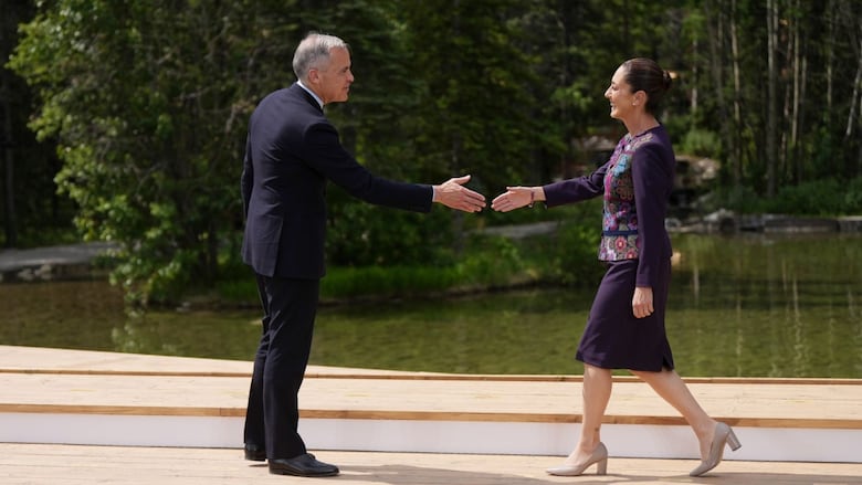 A man and woman reach out to shake hands on a photo podium outside.