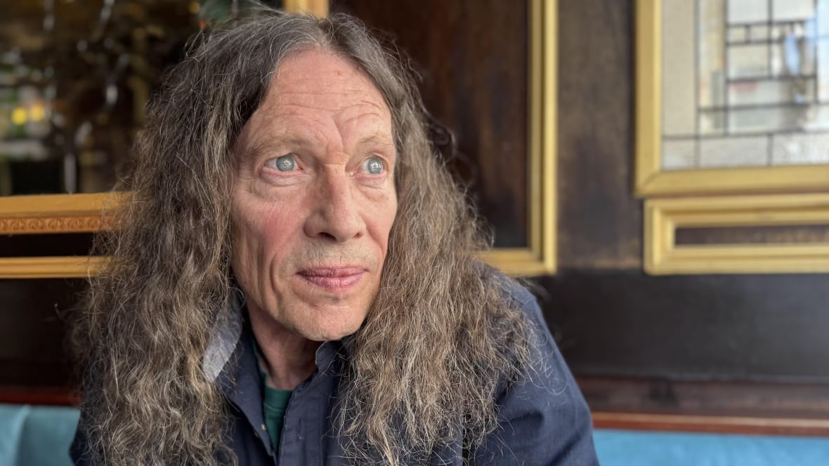 A man with long hair looks into the distance. 
