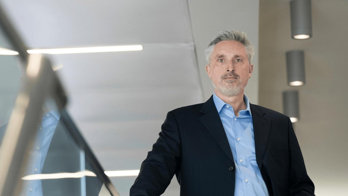 A man with grey hair in a suit looks into the camera