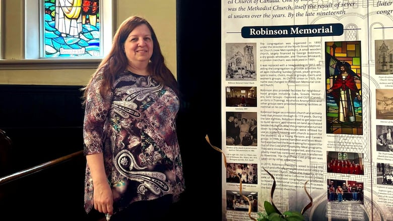 A woman stands inside a church with stained glass behind her