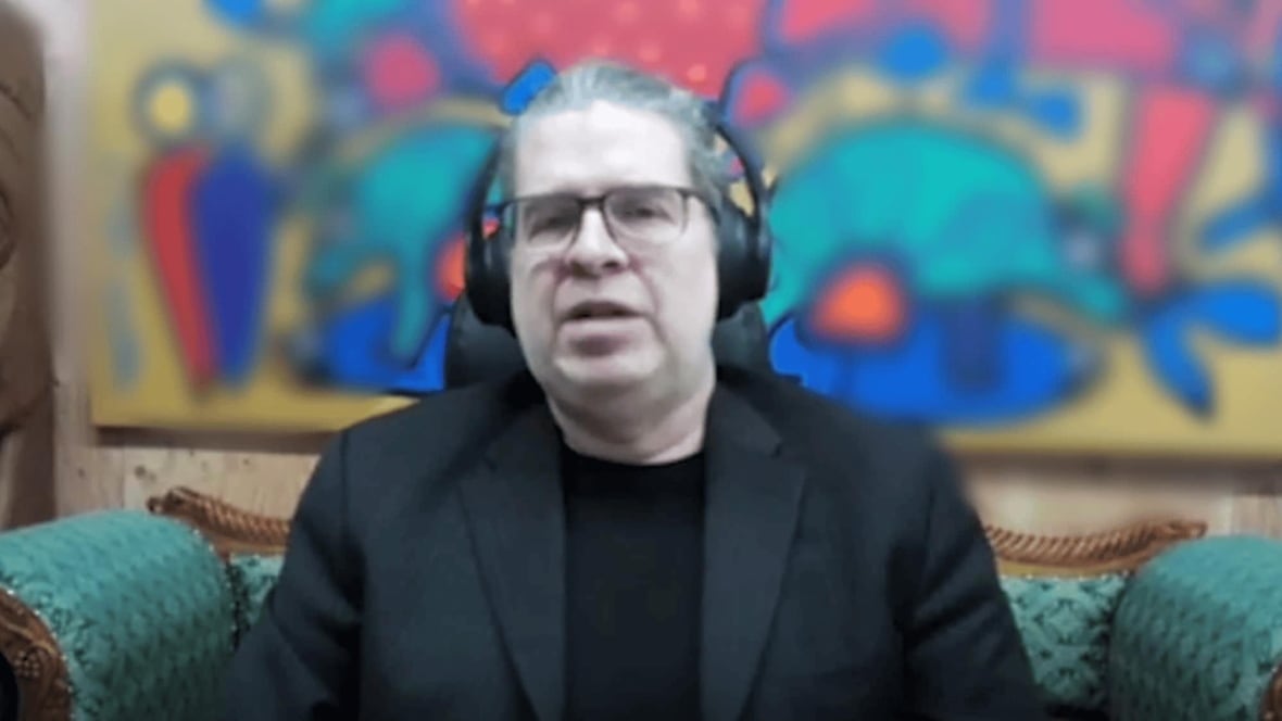 A man with headphones on speaks in front of a blurred background
