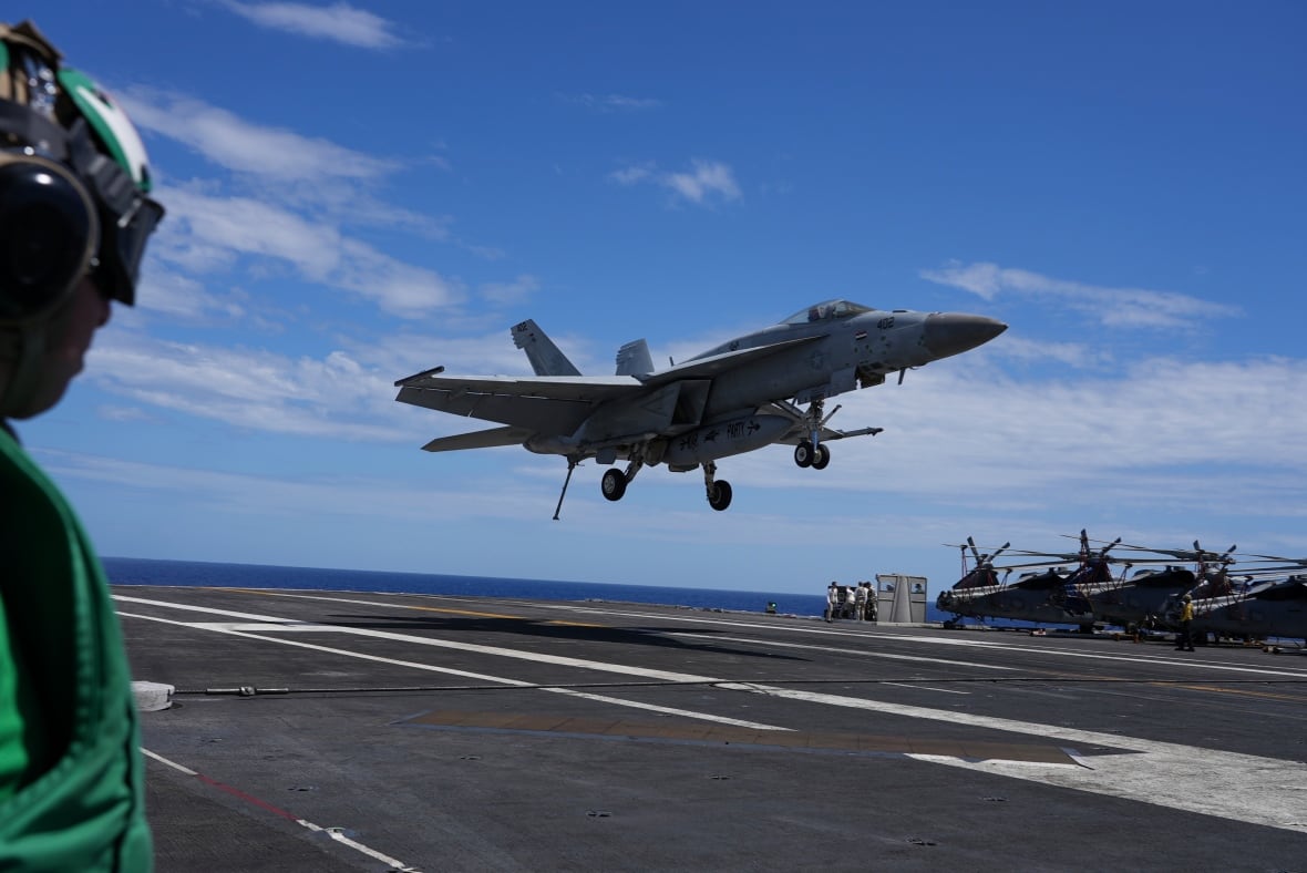 A fighter jet is seen taking off from a runway at sea.