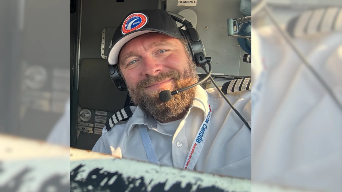 A man wearing a pilot uniform smiles at the camera.