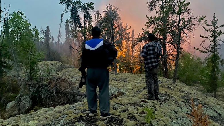 Two people stand watching near a small widlfire.