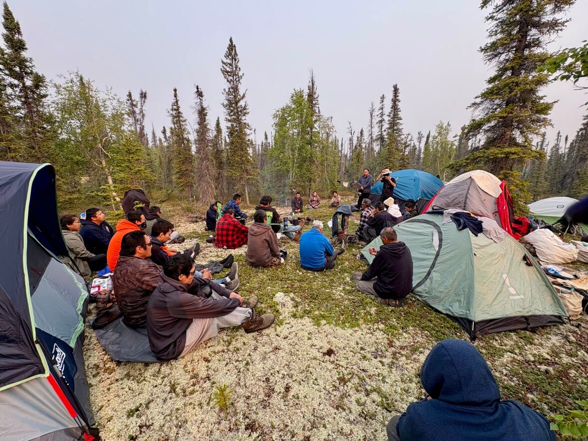 A group of people sitting on the ground among some camping tents.