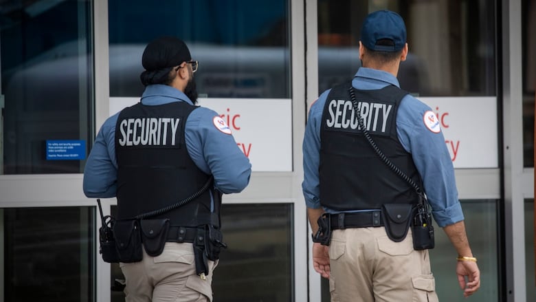 Two security guards in blue shirts walk outside a hospital.