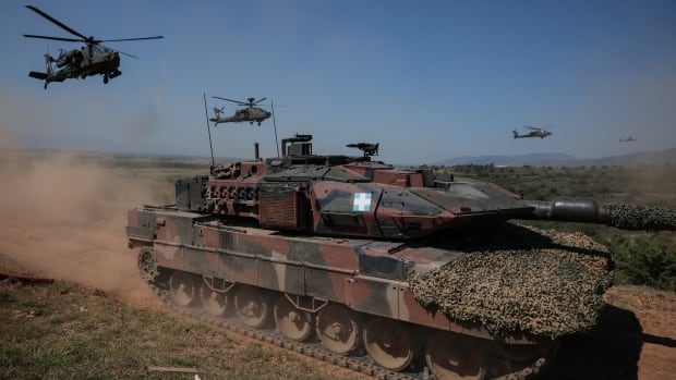 A tank and helicopters are seen in a dry landscape.